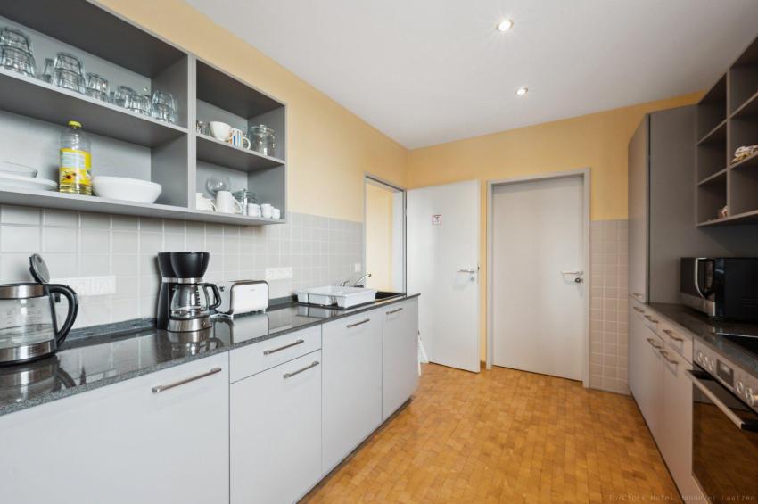 Küche mit Mikrowelle, Herd, Backofen, Ceranfeld, Kaffeemaschine, Spülmaschine, Kühlschrank, Gefrierfach, Teller, Besteck, Gläser, Tassen. 