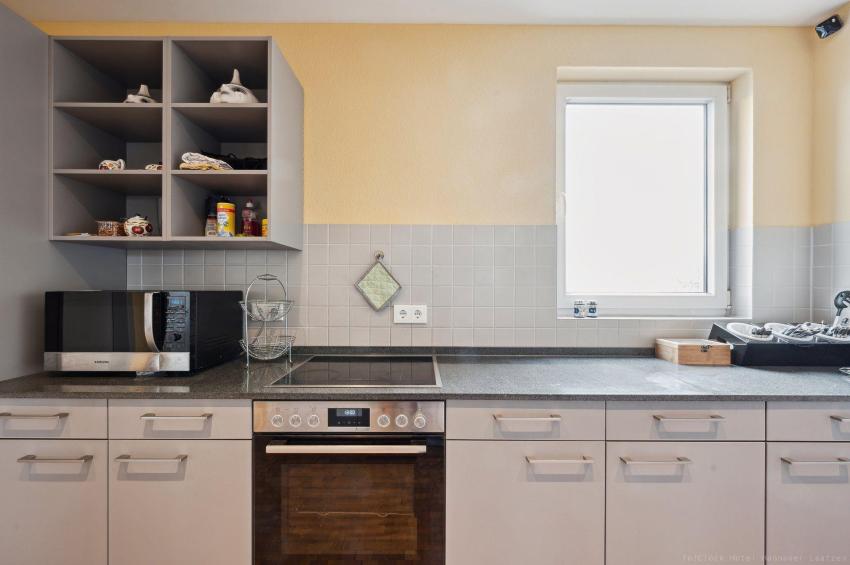 Küche mit Mikrowelle, Herd, Backofen, Ceranfeld, Kaffeemaschine, Spülmaschine, Kühlschrank, Gefrierfach, Teller, Besteck, Gläser, Tassen. 